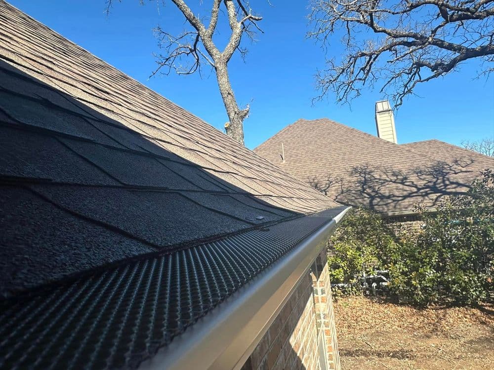 Roofline with shingles and guttering against a clear blue sky, showcasing home exterior details.