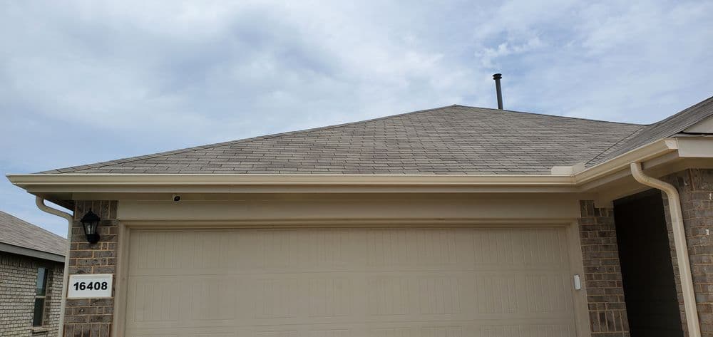 Roofline of a modern residential home with garage door and cloudy sky backdrop.