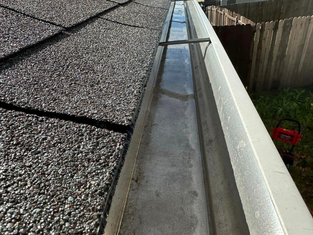 Gutter on a sloped roof with debris and water accumulation, sunshine highlighting details.