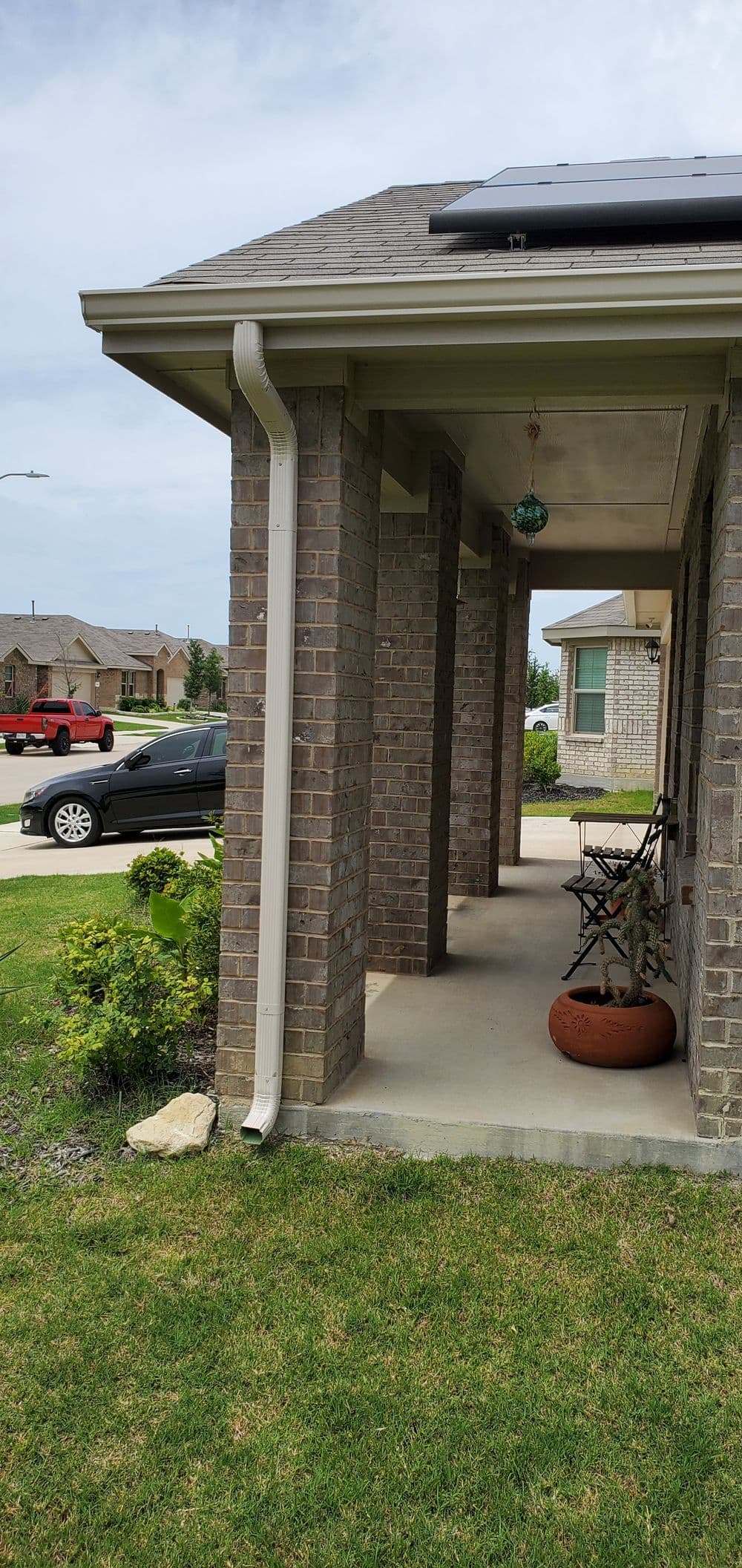 Front porch view of a brick house with a solar panel, seating, and landscaped lawn.
