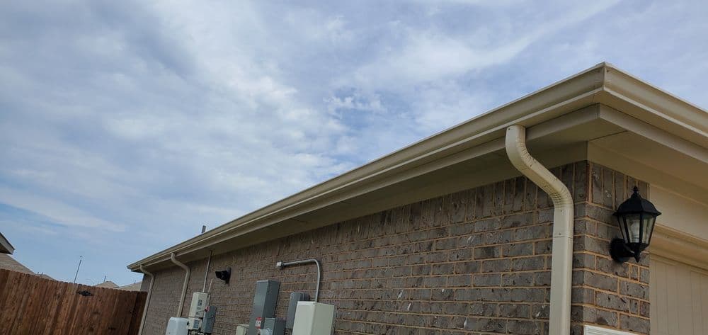 Residential home exterior with brick wall, electrical units, and cloudy sky overhead.