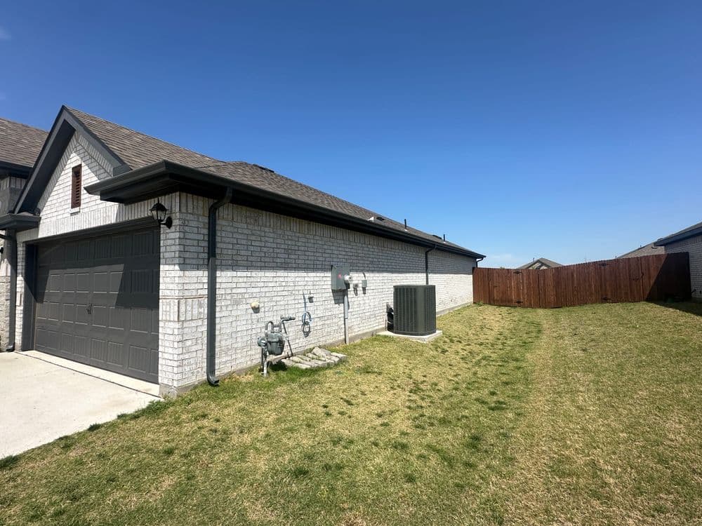 Side view of a modern house with gray garage, utility connections, and fenced yard.