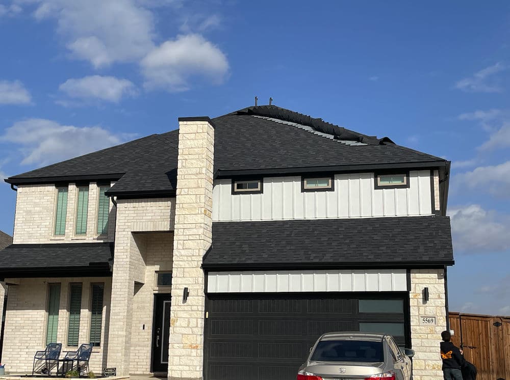 Modern two-story house with a new roof, featuring light stone and dark shingles.