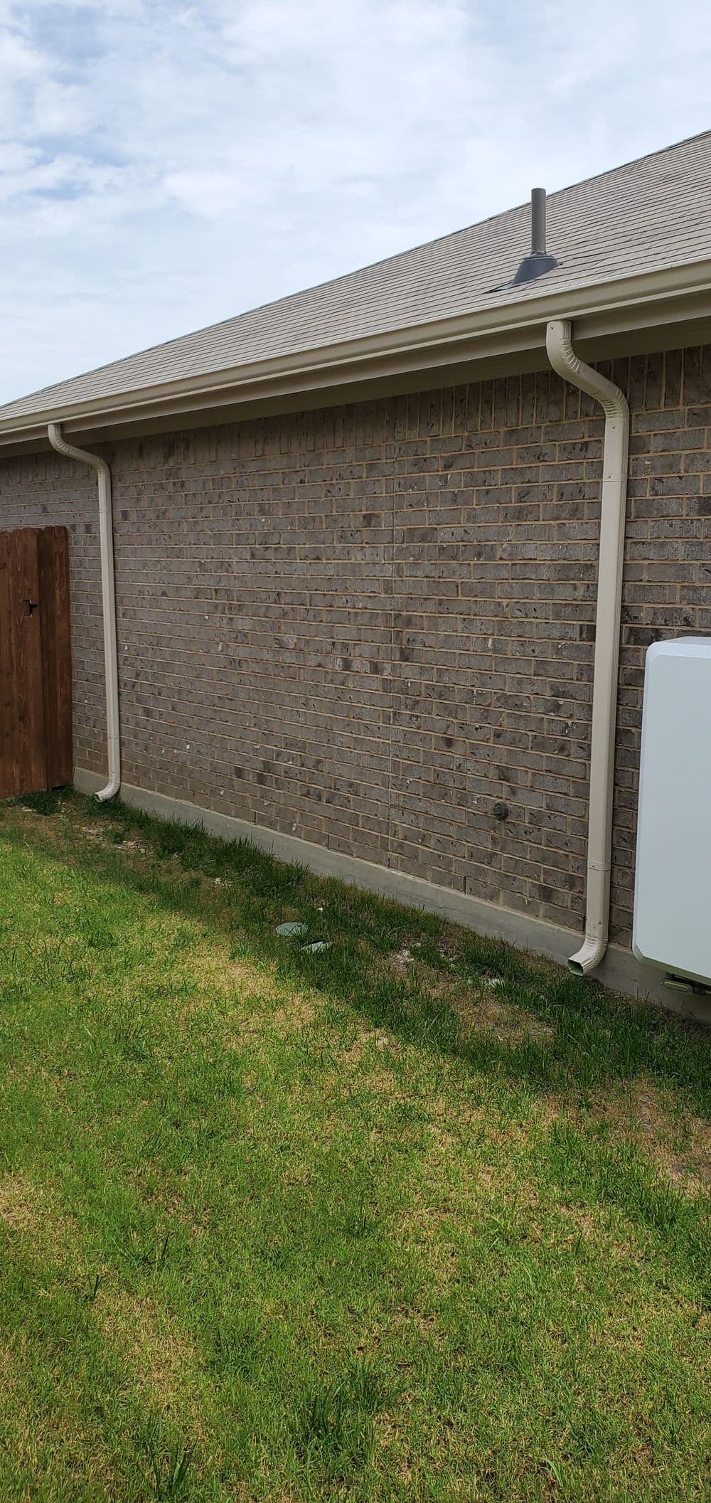 Side view of a brick house with rain gutters and a utility box on green lawn.