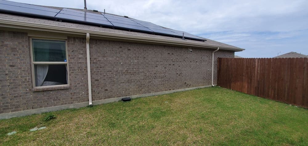 Home exterior with solar panels on the roof, grassy yard, and wooden fence.