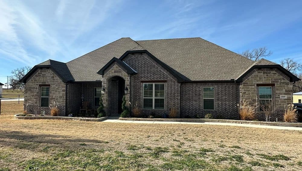 Modern brick house with a spacious front yard and large windows, featuring a gabled roof.
