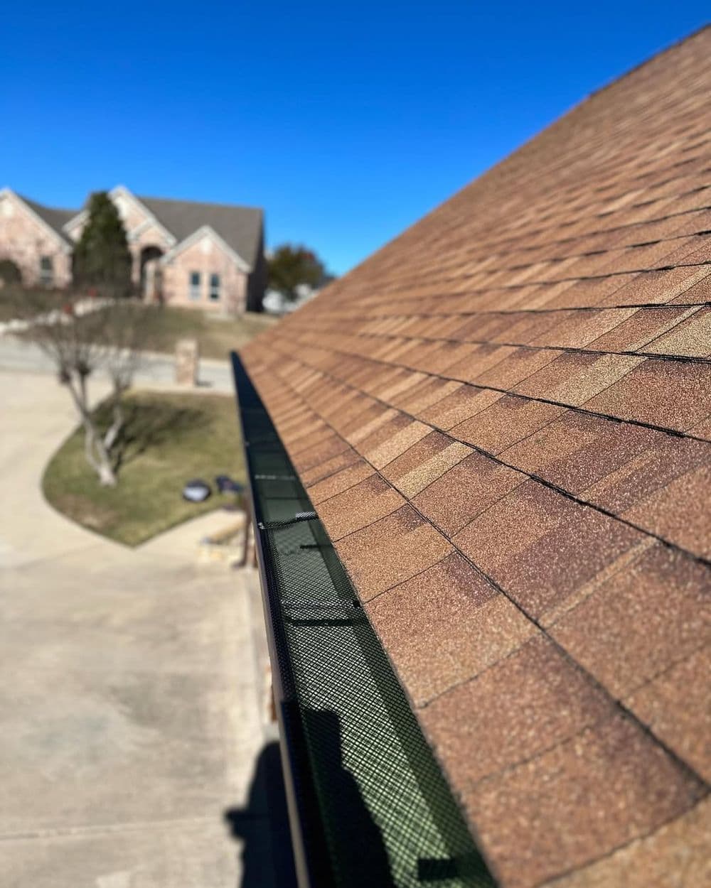 Brown asphalt shingles on a rooftop with a clear blue sky, showcasing a well-maintained roof.