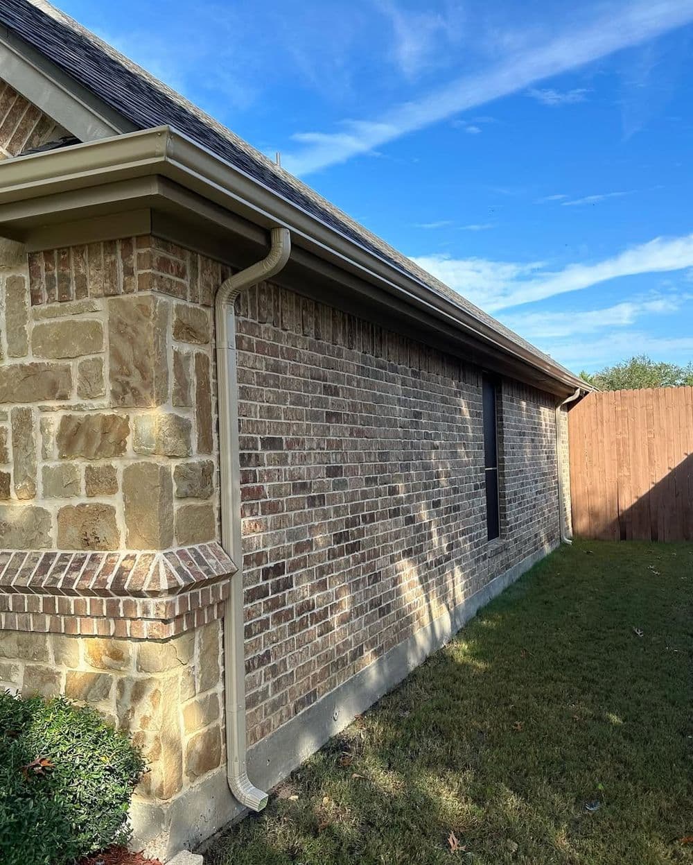 Residential brick house exterior with seamless gutters against a clear blue sky.