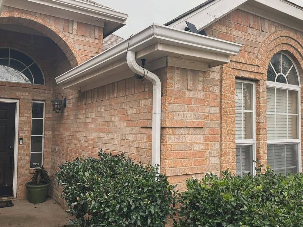 Brick home exterior with well-maintained bushes and drainage pipe detail.