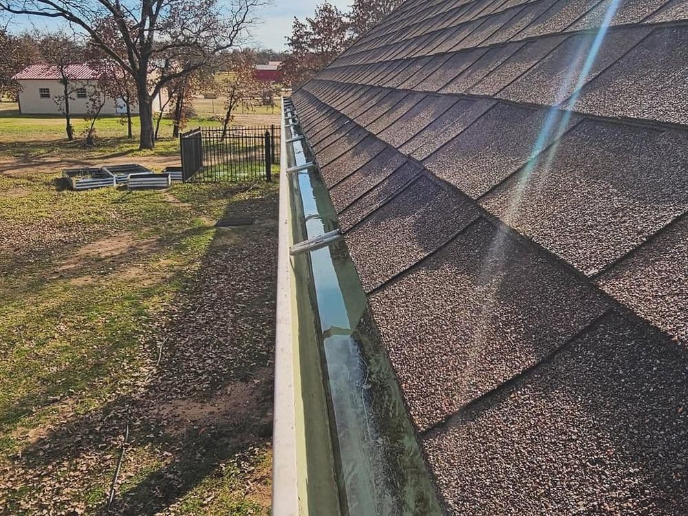 Gutter cleaning on a sloped roof with autumn leaves and a grassy yard in the background.