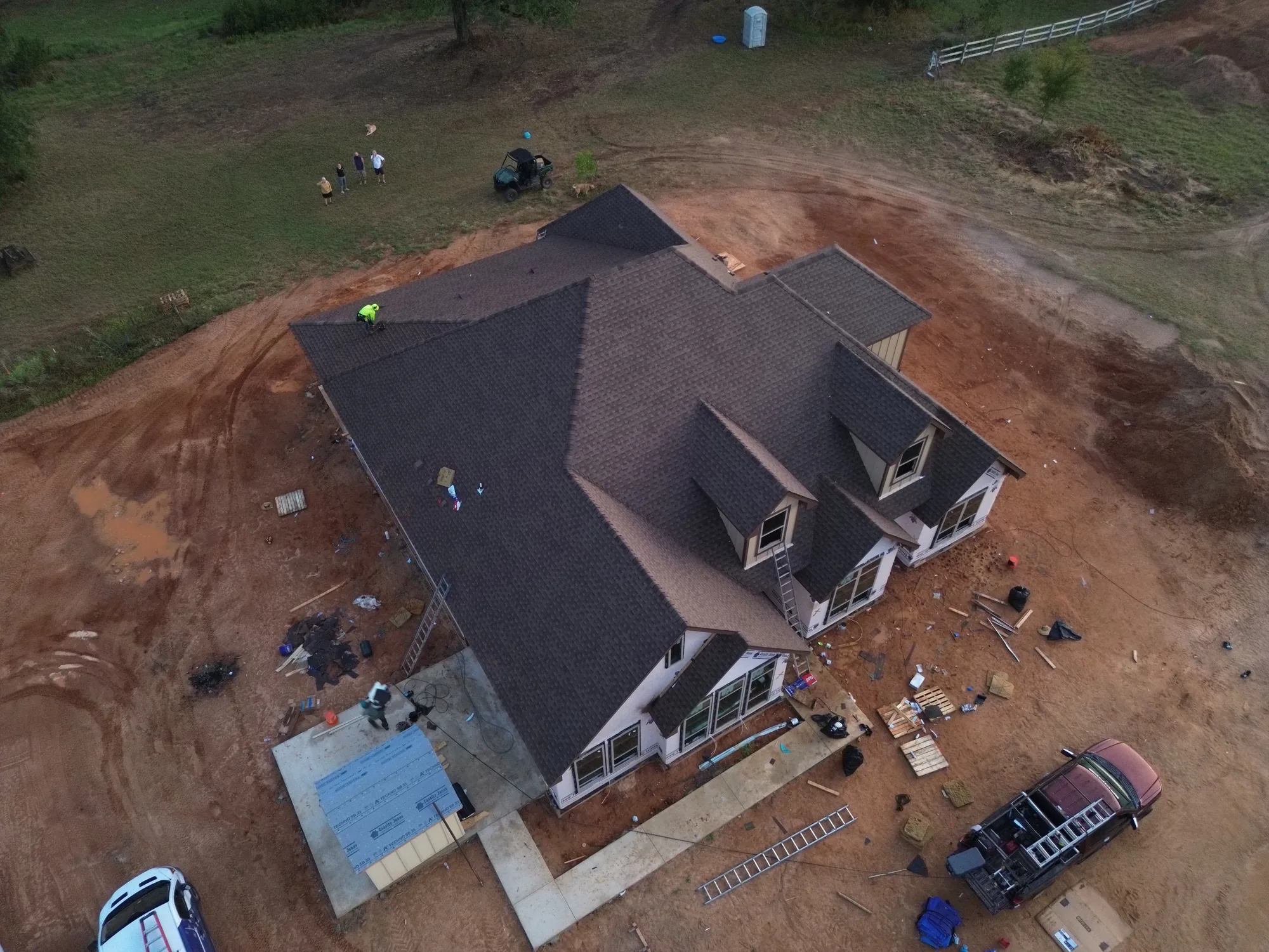 Drone view at dusk of a newly shingled home with dormers on a cleared red-dirt lot